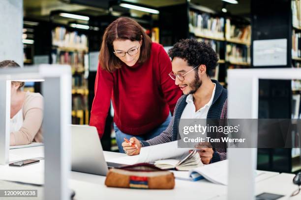 teacher helping student while working in public library - two men studying library stock-fotos und bilder