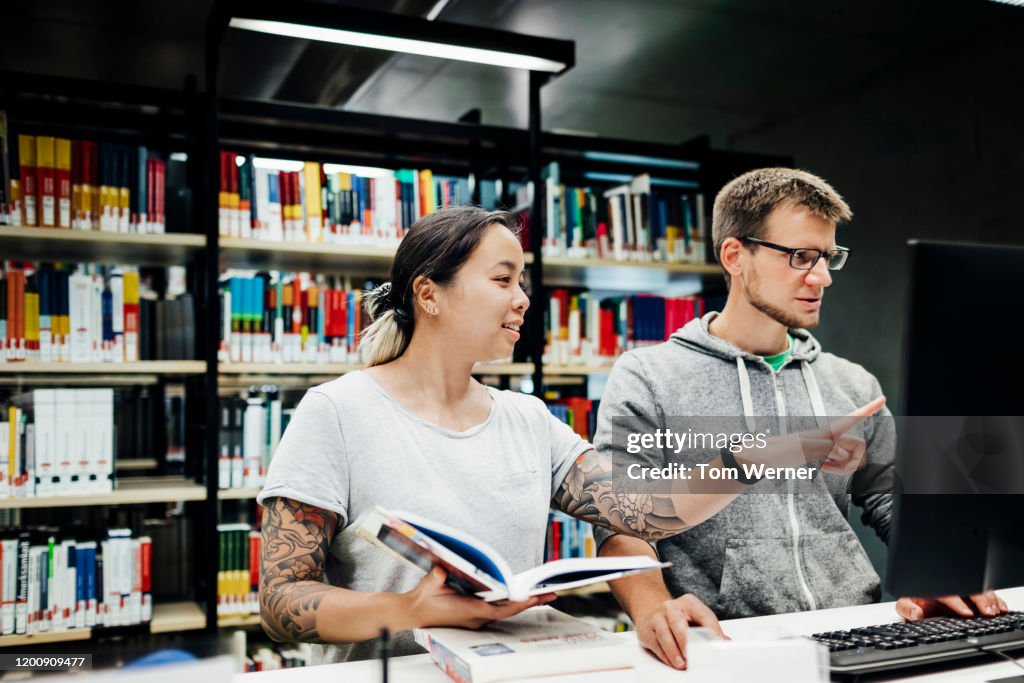 Two Friends Using Library Computer To Find Books