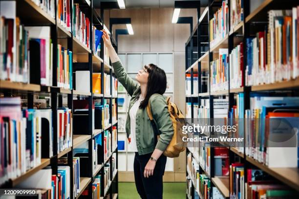 student selecting book from shelf in library - universiteit stockfoto's en -beelden