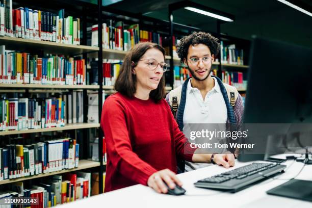 librarian looking up books on computer for student - bibliotecário imagens e fotografias de stock