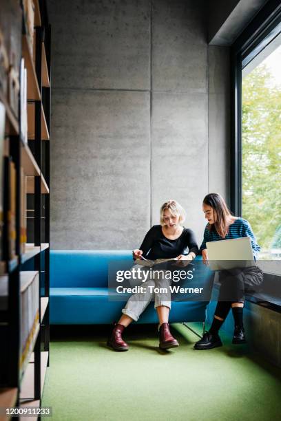 two friends working together in quiet library space - ensino superior imagens e fotografias de stock