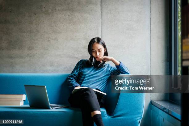 young woman sitting on couch in library - unterrichten stock-fotos und bilder