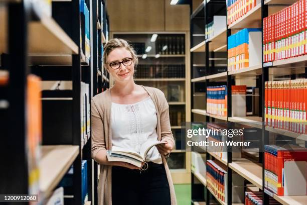 portrait of librarian leaning on bookshelf in library - bibliotecario foto e immagini stock