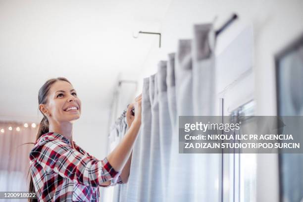 young housewife is hanging the curtains. - hanging stock pictures, royalty-free photos & images