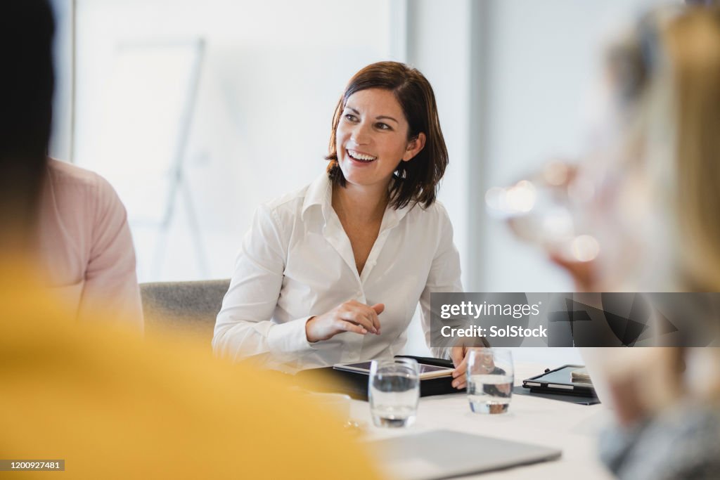 Vrolijke medio volwassen vrouw die bij bedrijfsvergadering glimlacht