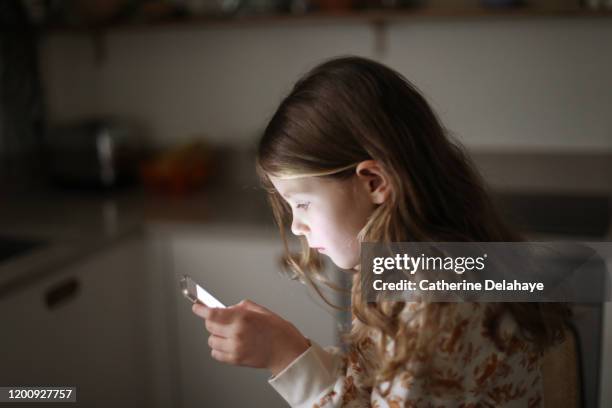 a 6 year old girl watching a phone in the kitchen - children screen stock-fotos und bilder