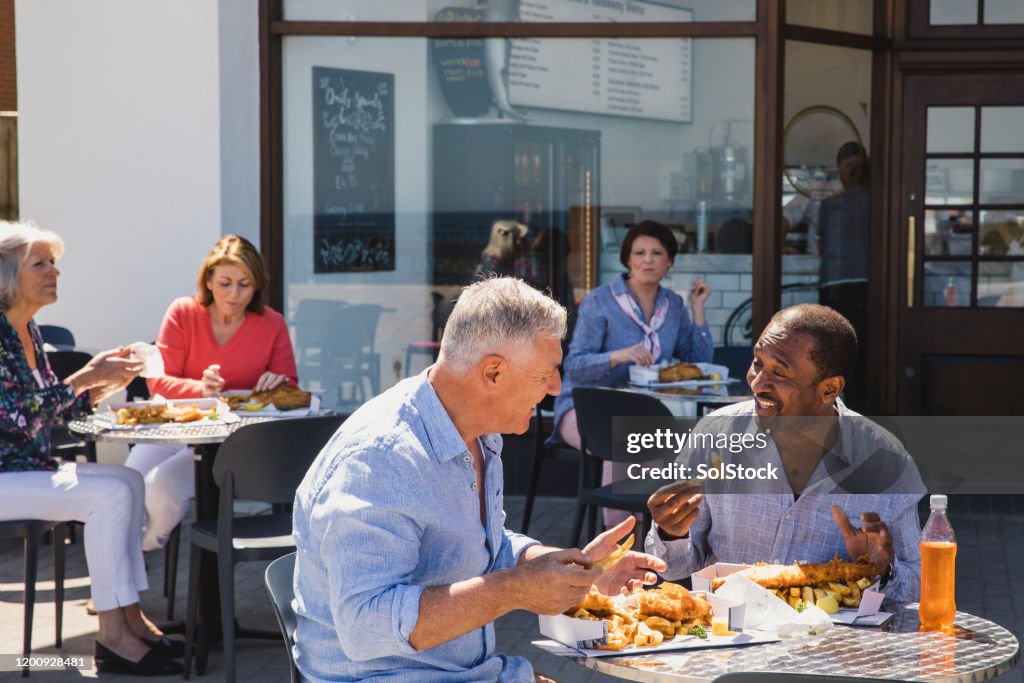 Senior male friends enjoying fish and chips outside cafe