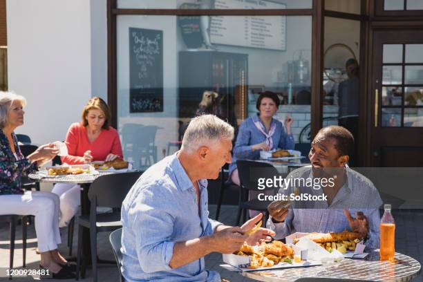 senior male friends enjoying fish and chips outside cafe - dining stock pictures, royalty-free photos & images