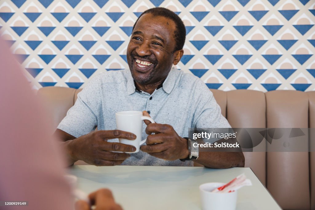 Cheerful senior man holding mug of coffee in cafe