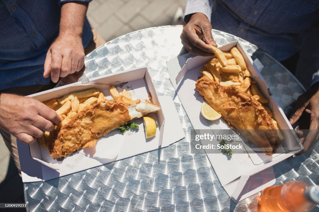 Overhead image of boxes of fish and chips being eaten outdoors