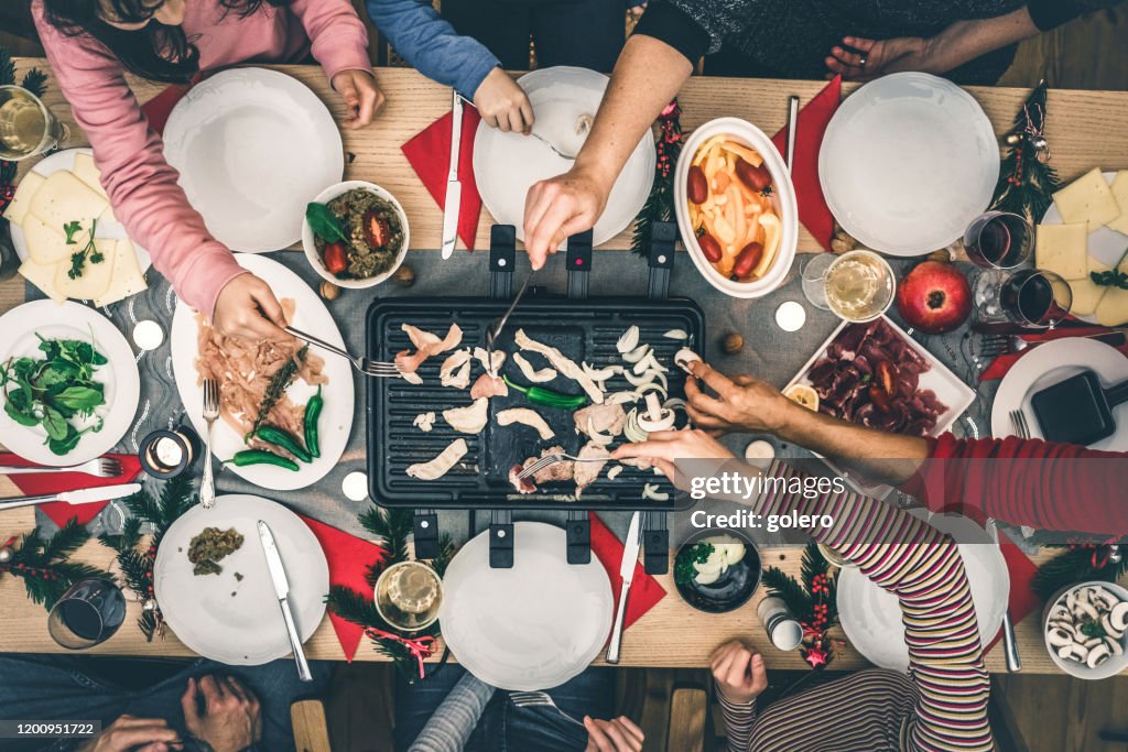 Familj förbereder olika rätter på raclette grill på träbord