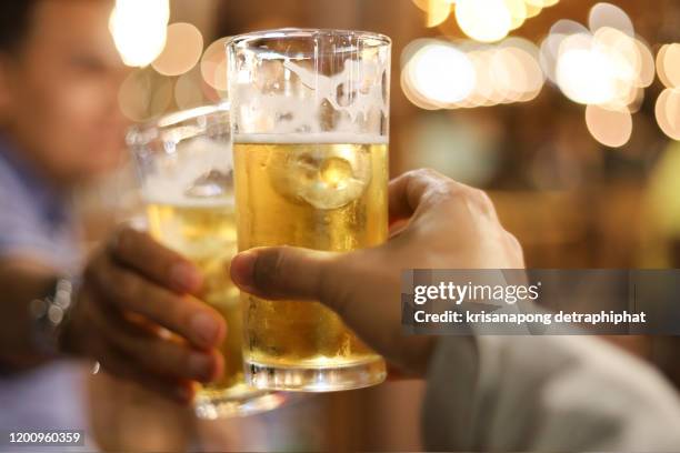 two glasses of beer cheers together between friend in the low light bar and restaurant. relax and drink concept,substance abuse - low alcohol drink stock pictures, royalty-free photos & images