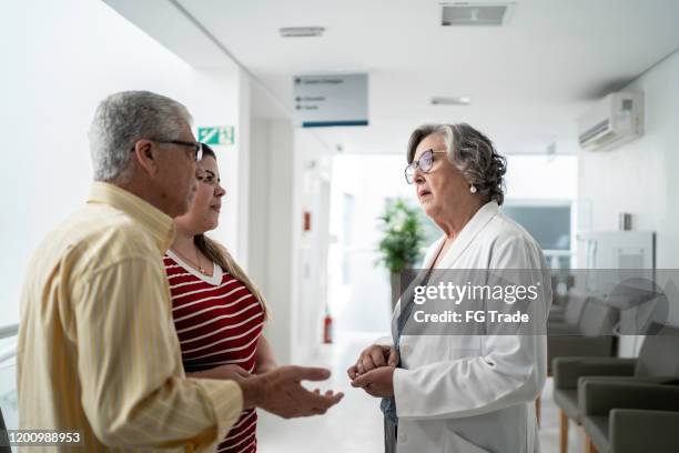 vrouwelijke hogere arts die over slecht nieuws en troostende droevige familie bij het ziekenhuis spreekt - family hospital old stockfoto's en -beelden