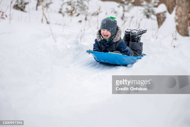 little boy sliding in the snow outdoors in winter - kids playing in snow imagens e fotografias de stock