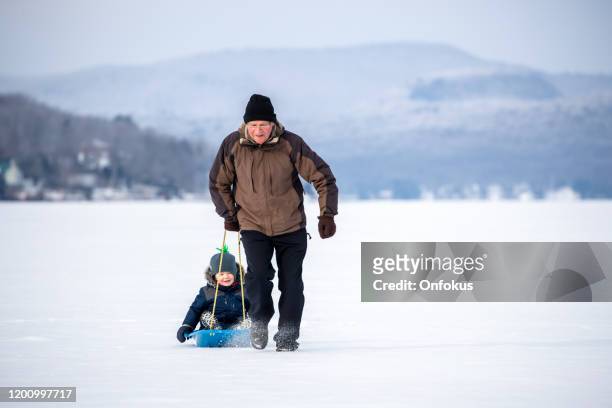 grandfather pulling grandson on sled on frozen lake in winter - grandfather child snow winter stock pictures, royalty-free photos & images