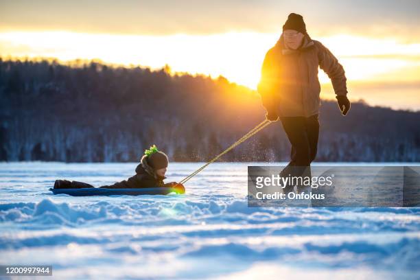 grootvader trekt kleinzoon op slee op bevroren meer in de winter bij zonsondergang - grandfather child snow winter stockfoto's en -beelden