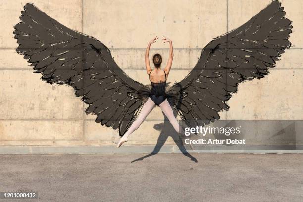 Creative picture of ballerina dancing with artistic black wings painted in the wall.