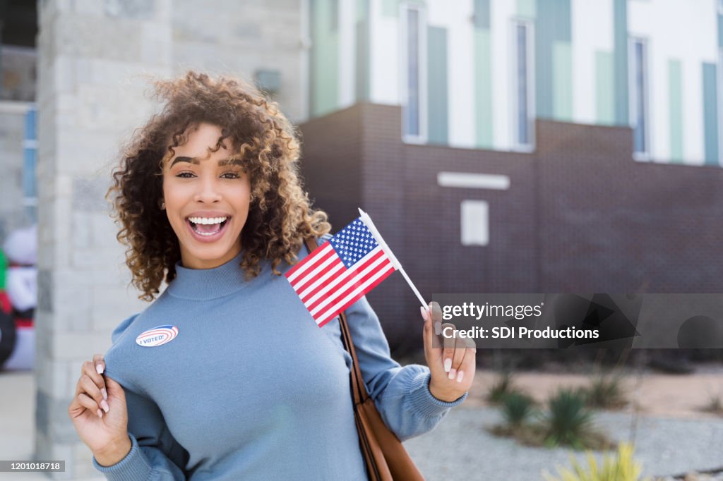 Mid adult woman displays "I Voted" sticker and American flag