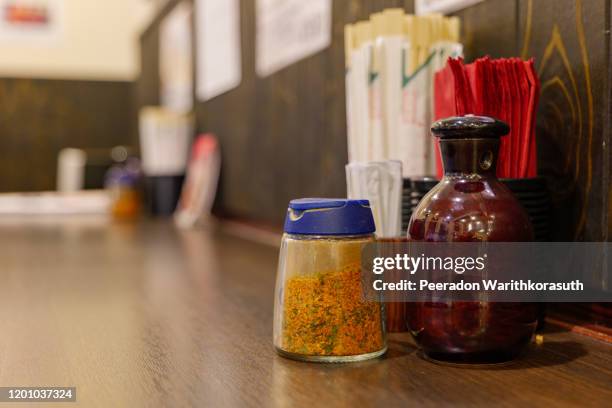 close up view of season bottles, with japanese red chili  flakes and soy sauce bottle, red napkins, chopsticks and toothpicks on wooden countertop of japanese restaurant. - restaurant düsseldorf stock-fotos und bilder