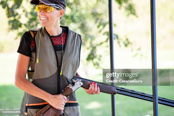 taille up portret van glimlachend volwassen vrouw na succes shot op shooting range houden haar shotgun-stockfoto - clay shooting stockfoto's en -beelden