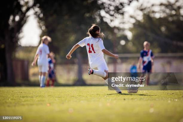 vista posteriore di una determinata giocatrice di calcio femminile che calcia la palla in una partita. - calcio sport foto e immagini stock