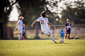 Rear view of determined female soccer player kicking the ball on a match.