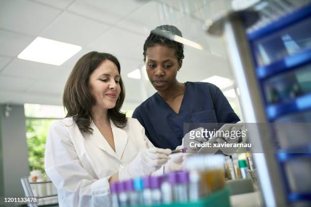 mujer patóloga y técnico examen de la prueba de tube muestra - inmunologia fotografías e imágenes de stock