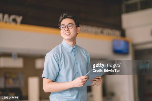 a portrait of asain chinese male medical healthcare worker in front of the entrance hall lobby corridor of hospital - man with clipboard imagens e fotografias de stock