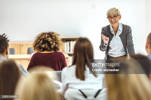 happy mature professor giving a lecture in front of her students at lecture hall. - female professor stock pictures, royalty-free photos & images