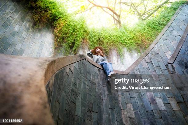 young asian traveler sitting in the big tree over tunnel and the stone wall and spiral staircase of fort canning park at singapore - singapore tourist stock pictures, royalty-free photos & images