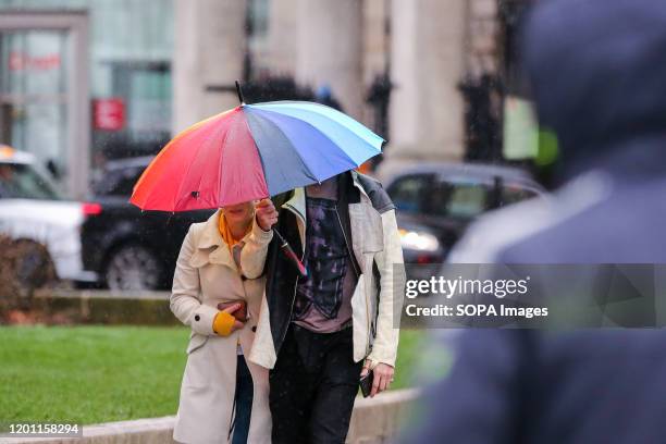 Couple under a coloured striped umbrella walk in central London during wet and windy weather. Storm Dennis will bring heavy rain and strong winds...