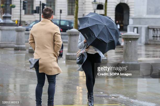 Woman struggles with an umbrella in central London during wet and windy weather. Storm Dennis will bring heavy rain and strong winds across the UK...