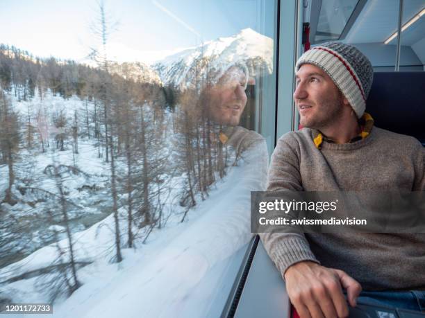 junger mann tourist mit zug in der schweiz mit blick durch fenster - winter travel stock-fotos und bilder