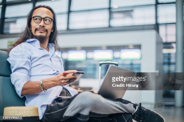 one mature man using laptop and credit card - airport corridor stock pictures, royalty-free photos & images