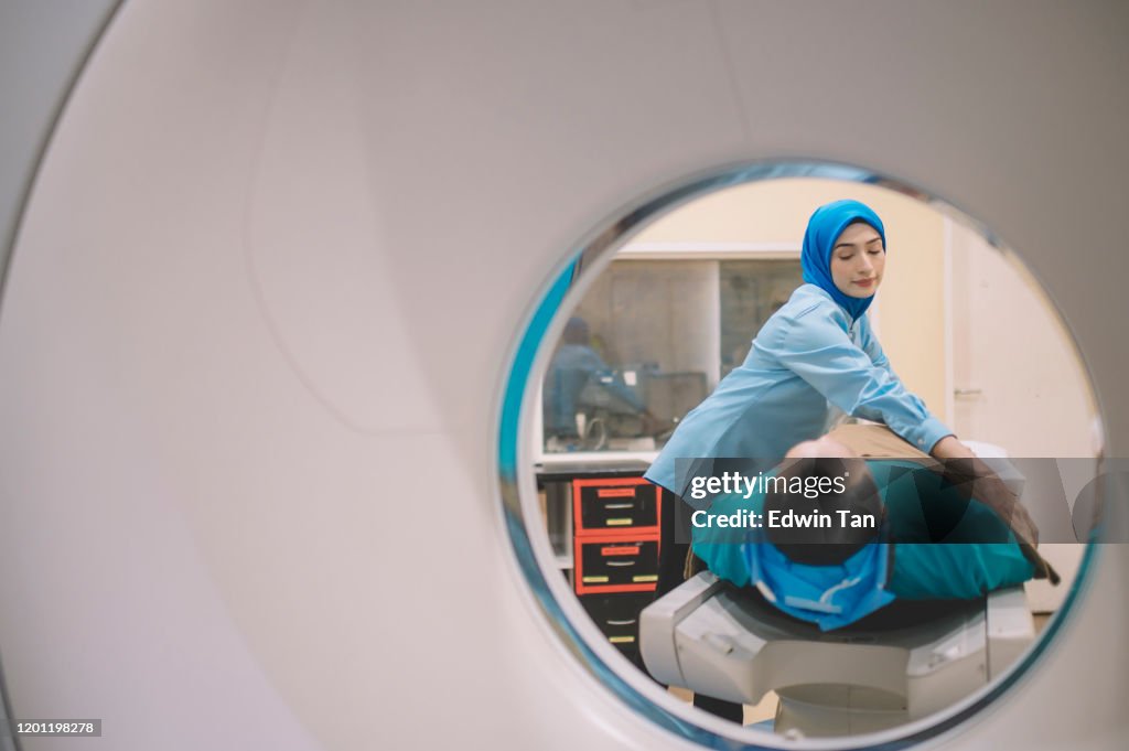 An asian malay male patient prepared for hospital CT Scan lying on the bed while a malay female nurse putting on a blanket for him