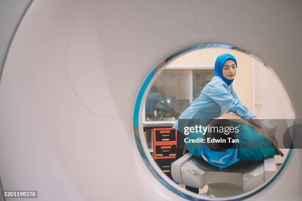 an asian malay male patient prepared for hospital ct scan lying on the bed while a malay female nurse putting on a blanket for him - skull xray no brain stock pictures, royalty-free photos & images