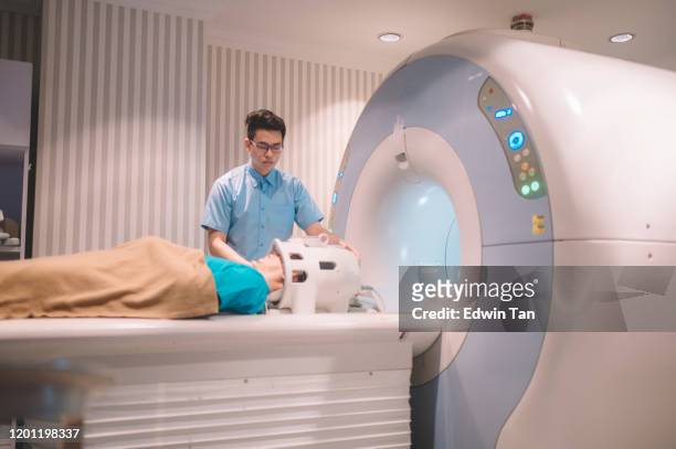 een aziatische chinese mannelijke verpleegster die zich klaar maakt om mri scan voor een mannelijke patiënt in de ruimte mri uit te voeren - mri scan medische scan stockfoto's en -beelden