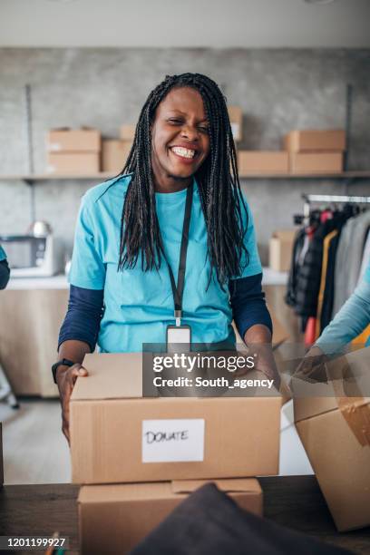 black woman volunteer packing donation boxes in charity food bank - clothing donations stock pictures, royalty-free photos & images