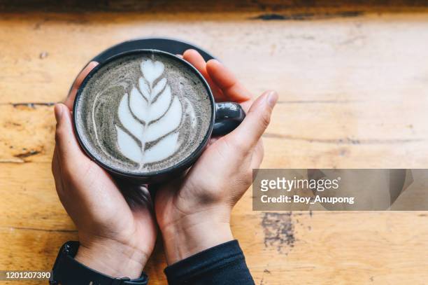 someone hands holding a cup of goth latte or charcoal latte on wooden table. - goth boy stock-fotos und bilder