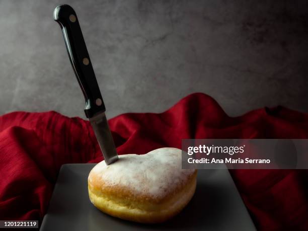 a knife stuck in a heart-shaped cake and sugar glass on top on a red cloth on a dark gray background - sugar kill foto e immagini stock