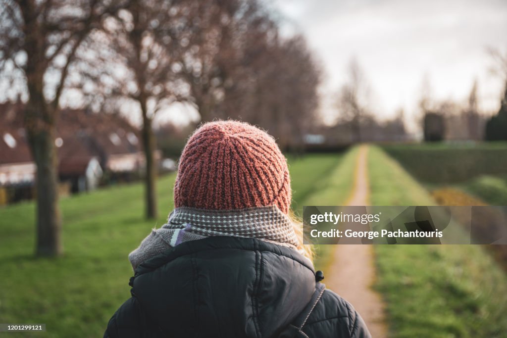 Woman walking on a narrow path dressed in warm clothes from behind
