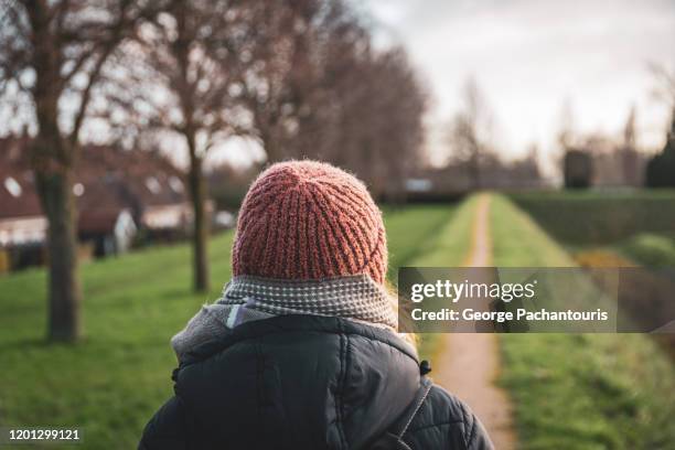 woman walking on a narrow path dressed in warm clothes from behind - koud stockfoto's en -beelden