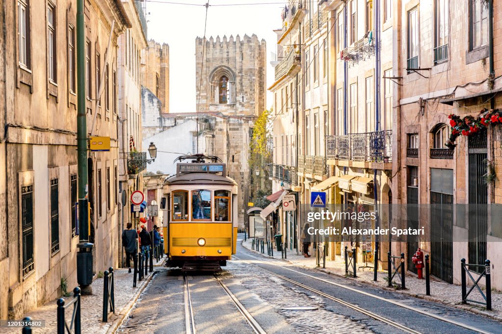 Street in Lisbon old town with yellow tram and Lisbon Cathedral in background, Lisbon, Portugal