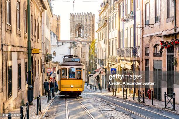 street in lisbon old town with yellow tram and lisbon cathedral in background, lisbon, portugal - lisbon fotografías e imágenes de stock