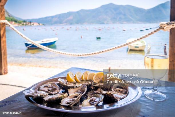 oysters in a white plate with lemon and a glass of wine on a wooden table isolated on white - adriatic sea stock pictures, royalty-free photos & images