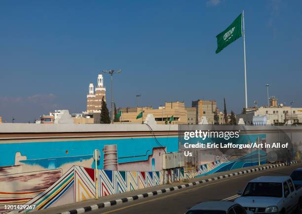 Saudi arabian flag in front of a fresco, Asir province, Abha, Saudi Arabia on January 3, 2020 in Abha, Saudi Arabia.