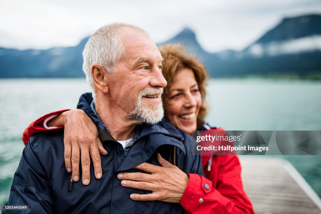 Senior couple tourist standing by lake in nature on holiday, hugging.