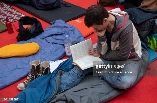 February 2020, Berlin: A man is sitting reading on a sleeping mat and sleeping bag in the Potsdamer Platz Arkaden, waiting for the start of ticket...