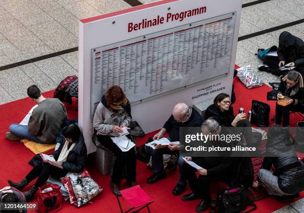 February 2020, Berlin: Film lovers are waiting in the Potsdamer Platz Arkaden next to a board with the words "Berlinale Programme" for the start of...