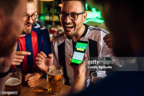 amici che bevono birra, guardano la partita di calcio e usano l'app mobile per le scommesse - calcio sport foto e immagini stock